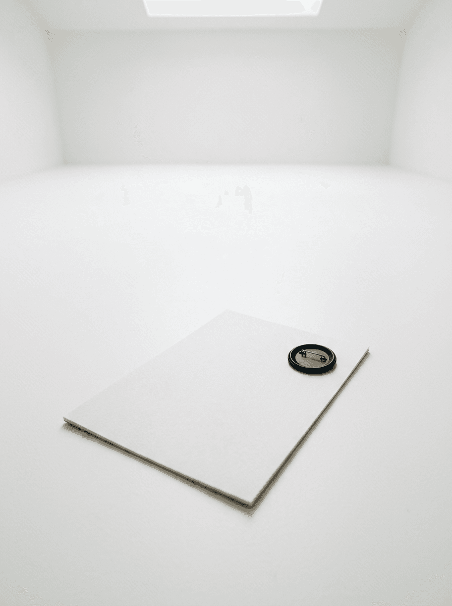 A blank sheet of paper with a black badge pinned to it on a white floor